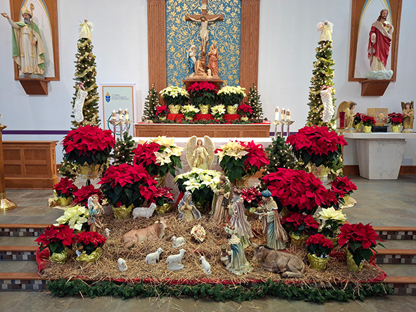 nativity scene at altar with figurines, straw, and poinsettias